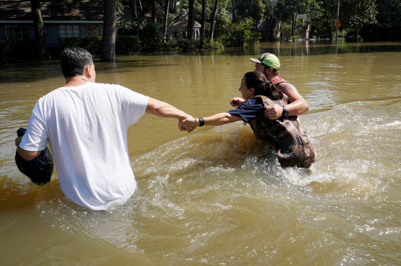 © Reuters. Melissa Ramirez struggles against the current flowing down a flooded street helped by Edward Ramirez and Cody Collinsworth as she tried to return to her home for the first time since Harvey floodwaters arrived in Houston