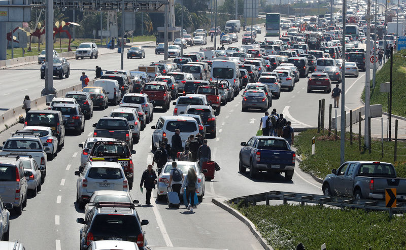 © Reuters. People walk through traffic along a highway as taxi drivers block the way to Santiago's international airport during a protest against Uber and Cabify technologies in Santiago