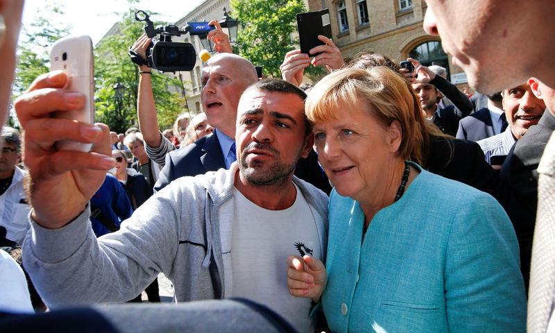 © Reuters. FILE PHOTO: A migrant takes a selfie with German Chancellor Merkel outside a refugee camp near the Federal Office for Migration and Refugees after registration at Berlin's Spandau district