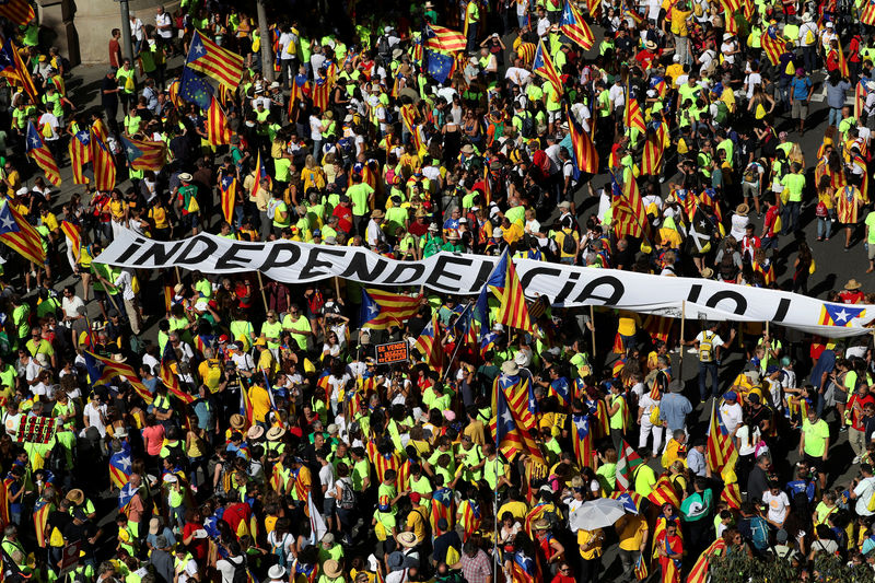 © Reuters. A man carries a sign that reads "Spain for sale" next to a huge banner reading "Independence Now" during a rally on Catalonia's national day 'La Diada' in Barcelona