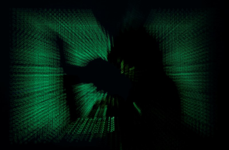 © Reuters. Hooded man holds laptop computer as cyber code is projected on him in this illustration picture