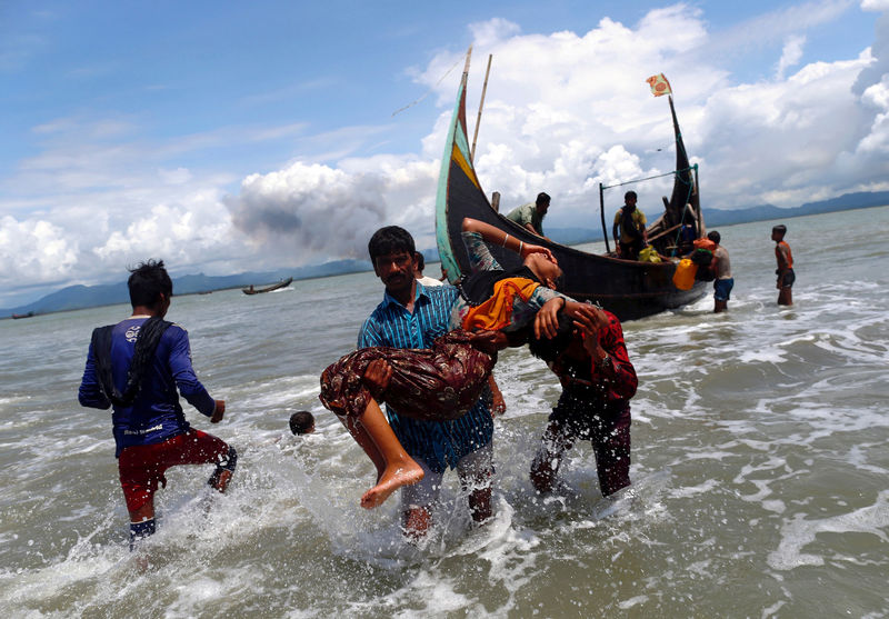 © Reuters. FILE PHOTO: Smoke is seen on Myanmar's side of border as an exhausted Rohingya refugee woman is carried to the shore after crossing the Bangladesh-Myanmar border by boat through the Bay of Bengal, in Shah Porir Dwip