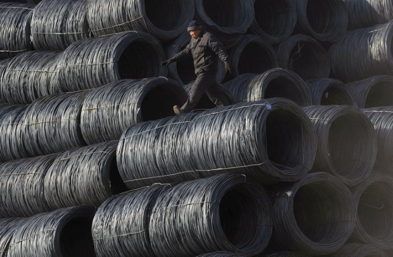 © Reuters. A labourer walks on coils of steel wire at a steel market in Shenyang