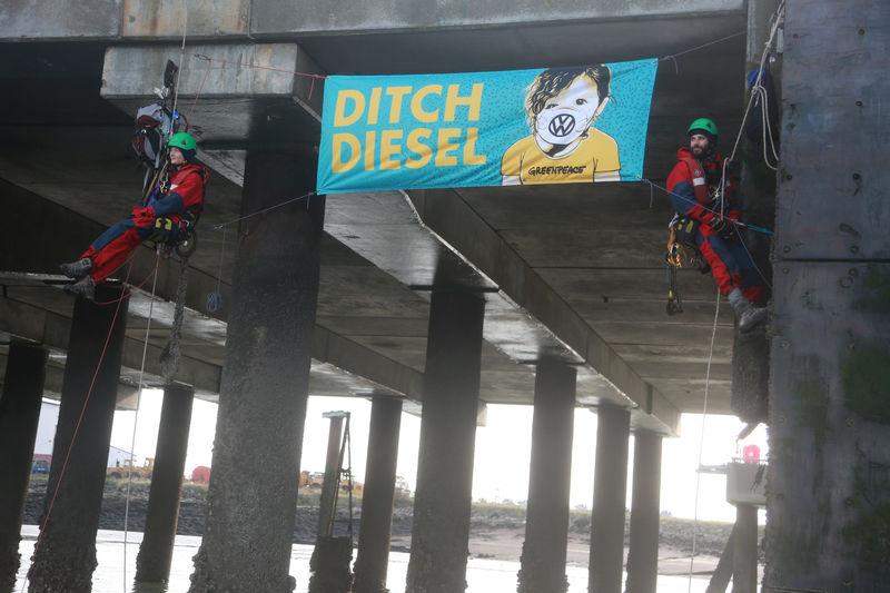 © Reuters. Greenpeace volunteers hang next to a banner after others boarded a ship carrying Volkswagen vehicles for import sailing up the Thames Estuary towards the port of Sheerness
