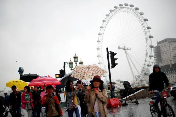 © Reuters. Tourists carrying umbrellas shelter from the rain in front of the London Eye wheel in London