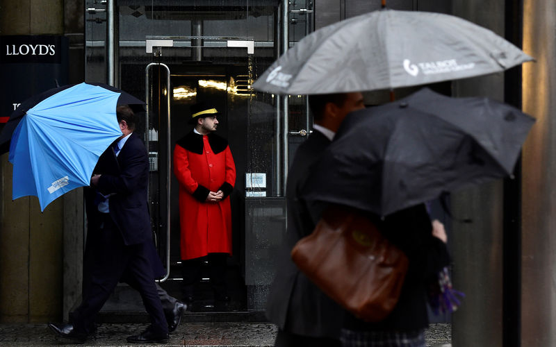 © Reuters. FILE PHOTO: A doorman looks out as workers walk in the rain past the Lloyd's of London building in the City of London