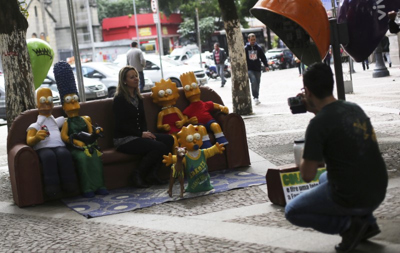 © Reuters. A tourist poses for a photo with figurines of the characters from the television show "The Simpsons", along a street in Sao Paulo