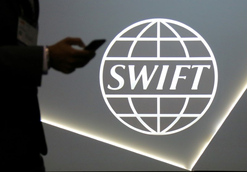 © Reuters. FILE PHOTO: A man using a mobile phone passes the logo of global secure financial messaging services cooperative SWIFT at the SIBOS banking and financial conference in Toronto