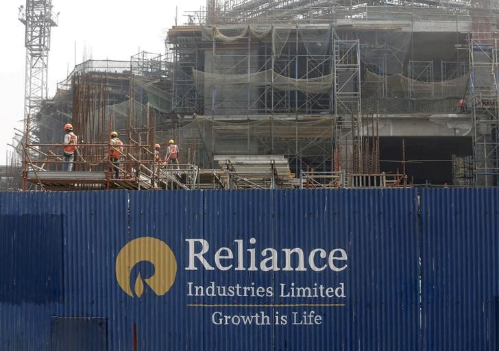 © Reuters. FILE PHOTO: Labourers work behind an advertisement of Reliance Industries Limited at a construction site in Mumbai