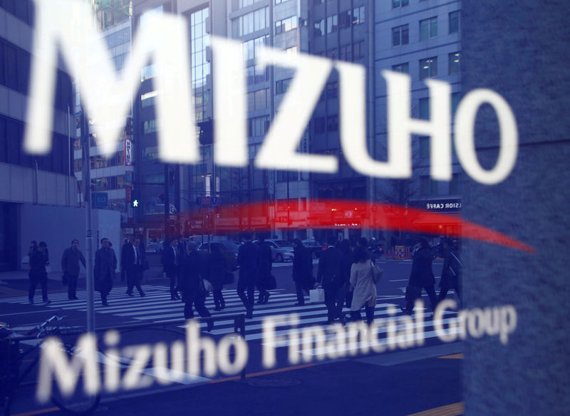 © Reuters. FILE PHOTO: Pedestrians are reflected on Mizuho Bank's signboard in Tokyo