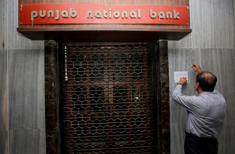 © Reuters. A man tries to remove a notice pasted on the wall of a Punjab National Bank branch after it was sealed by India's federal police in Mumbai
