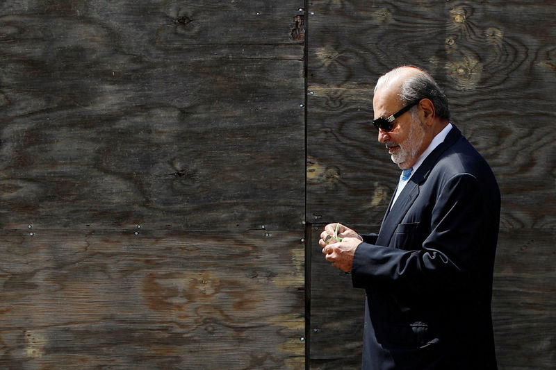 © Reuters. Mexican billionaire Carlos Slim holds money as he walks on a street after attending a ceremony to place the first stone of the new U.S. Embassy, in Mexico City
