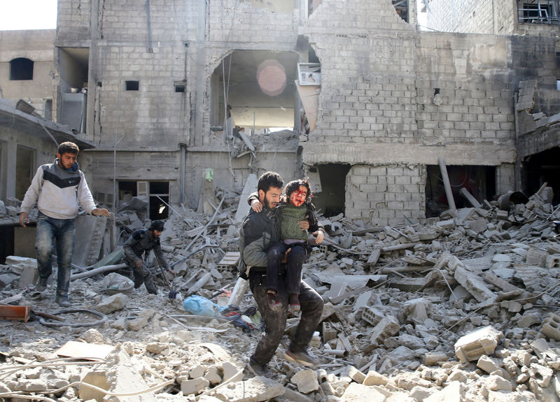 © Reuters. Homem carrega menino ferido em meio a destroços na cidade de Hamouriyeh, em Ghouta Oriental, na Síria