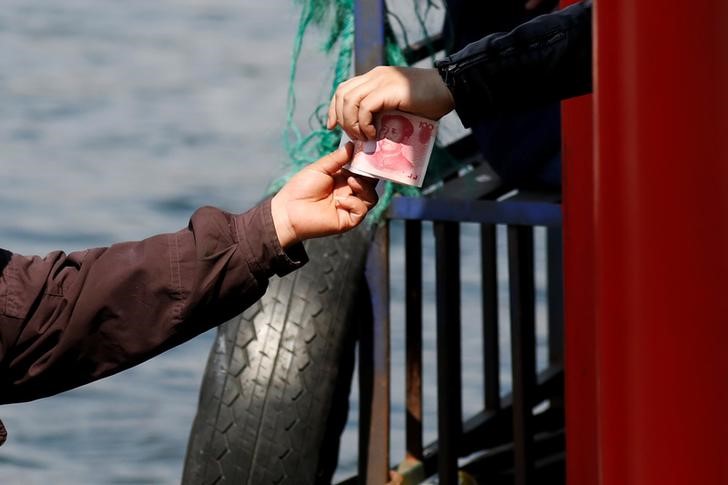 © Reuters. A vendor receives Chinese banknotes after selling North Korean goods to tourists on a boat taking them from the Chinese side of the Yalu river for sightseeing close to the shores of North Korea near Dandong