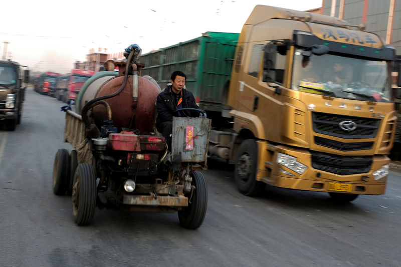 © Reuters. FILE PHOTO: A worker drives a motorised vehicle past trucks parked outside ceramics factories in rural Gaoyi county near Shijiazhuang