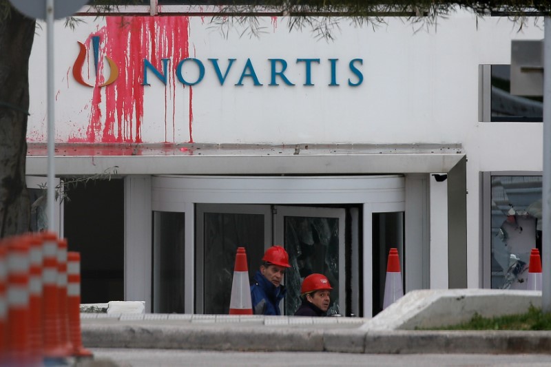 © Reuters. Workers clean the entrance of the Swiss drugmaker Novartis offices after protesters threw paint and smashed windows, in Athens