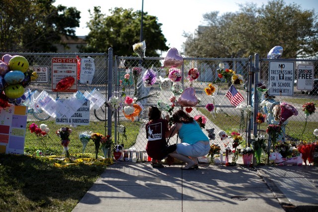 © Reuters. People put flowers among other mementoes at the fence of the Marjory Stoneman Douglas High School, after the police security perimeter was removed, following a mass shooting in Parkland