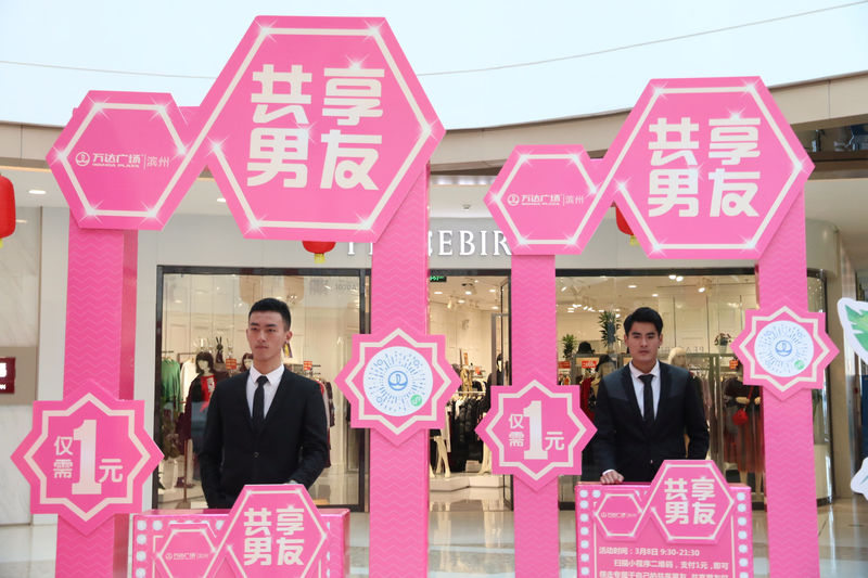 © Reuters. Men stand behind booths during an International Women's Day event inside a shopping mall, where customers can rent a "shared boyfriend" for one yuan ($0.16), in Binzhou, Shandong