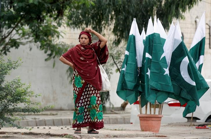 © Reuters. A woman adjusts her scarf as she waits for a bus next to a stall with national flags, ahead of Pakistan's Independence Day, in Karachi