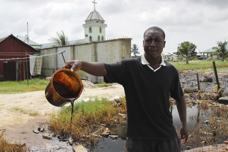 © Reuters. A villager shows a bucket of of crude oil spill at the banks of a river, after a Shell pipeline leaked, in the Oloma community in Nigeria's delta region