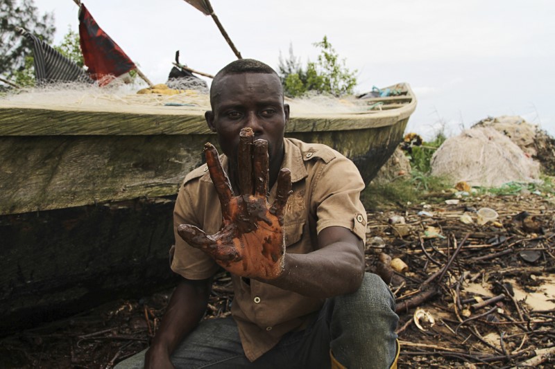 © Reuters. Un pescatore mostra il catrame sul palmo della sua mano dopo averla immersa nelle acque del delta del Niger
