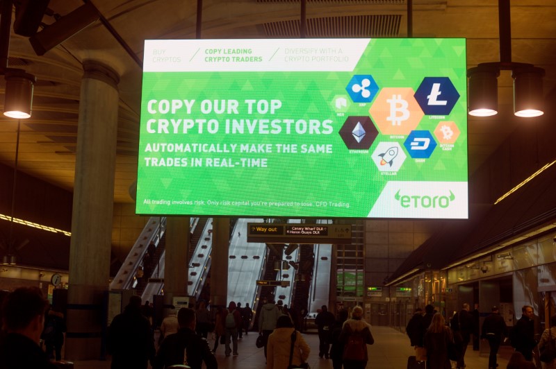 © Reuters. Giant electronic billboards display adverts for crypto currency investment companies as commuters arrive at Canary Wharf tube station in London