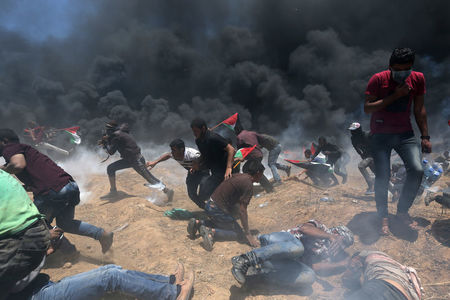 © Reuters. Manifestanti palestinesi oggi alla frontiera con Israele, mentre cercano di mettersi al riparo dai colpi d'arma da fuoco e dai gas lacrimogeni sparati dalle forze israeliane