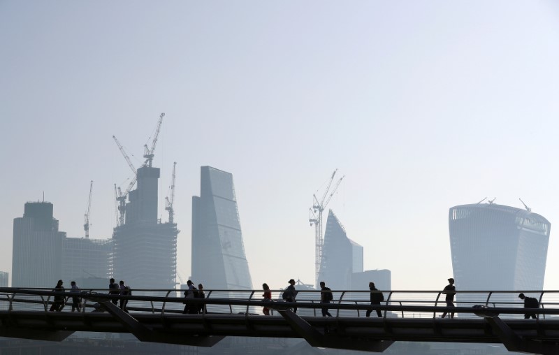 © Reuters. FILE PHOTO: People cross the Millenium Bridge in front of the City on a sunny morning in London
