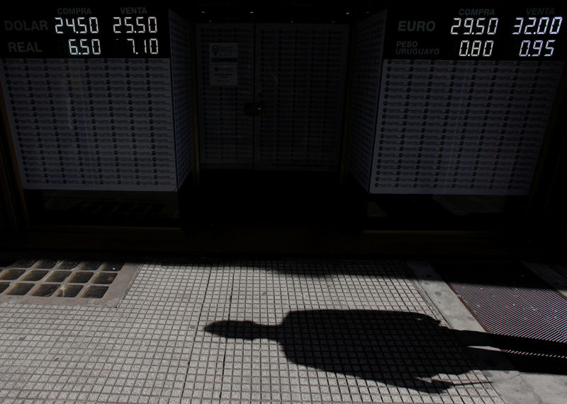 © Reuters. A pedestrian's shadow is cast next to an electronic board showing currency exchange rates in Buenos Aires