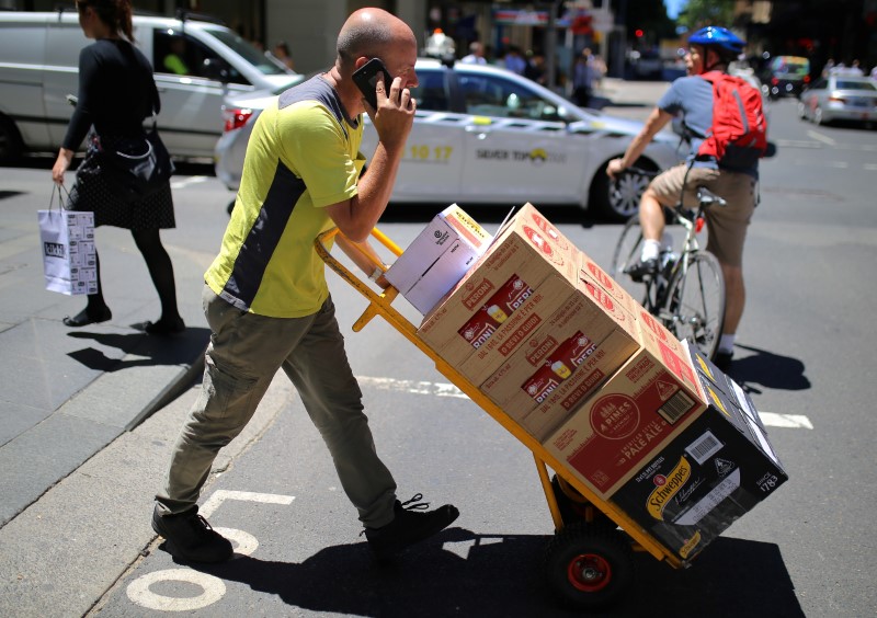 © Reuters. A worker talks on his phone as he pushes a trolley loaded with goods across a main road in a retail shopping area in central Sydney