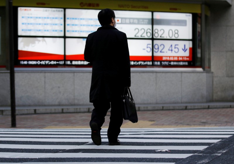 © Reuters. FILE PHOTO: Man walks past an electronic board showing Japan's Nikkei average outside a brokerage in Tokyo