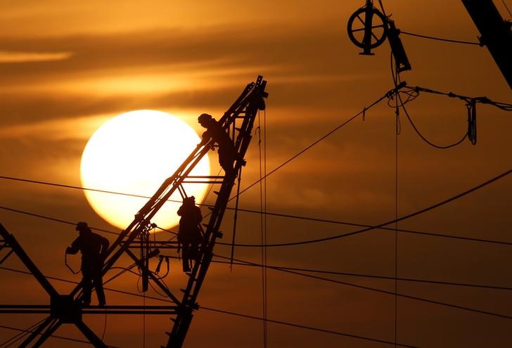 © Reuters. Technicians work on an electricity pylon as part of maintenance of high-tension electricity power lines, during sunset in Cantin