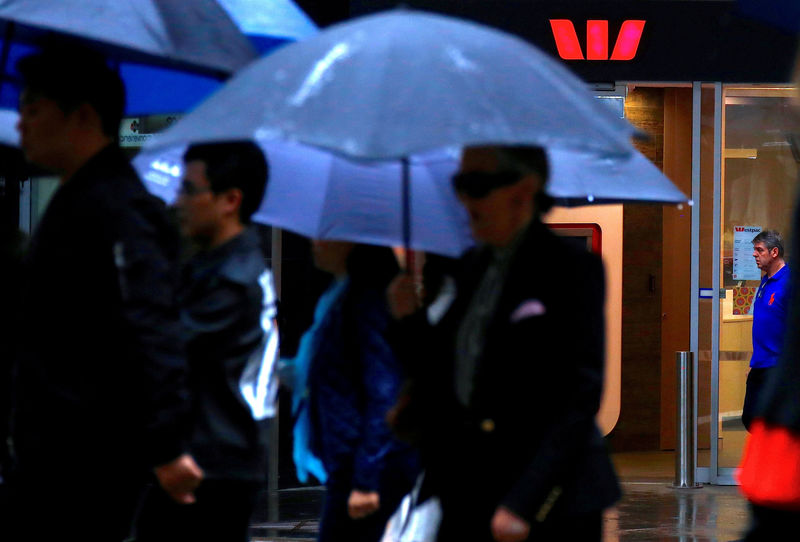 © Reuters. FILE PHOTO: Pedestrians hold umbrellas as they walk past a branch of the Westpac Banking Corp in central Sydney, Australia