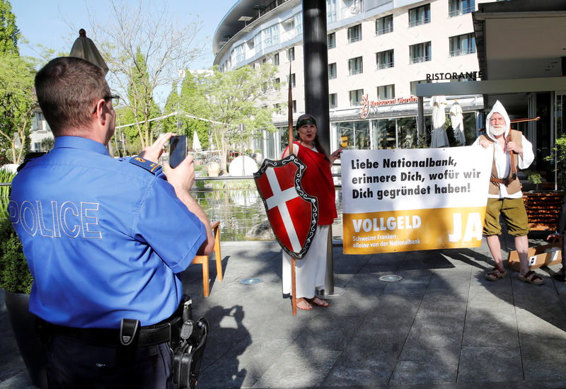 © Reuters. FILE PHOTO: A policeman takes a pictures of members of the sovereign money initiative dressed as Helvetia and William Tell, during a demonstration outside the Shareholders meeting of the Swiss National Bank (SNB) in Bern