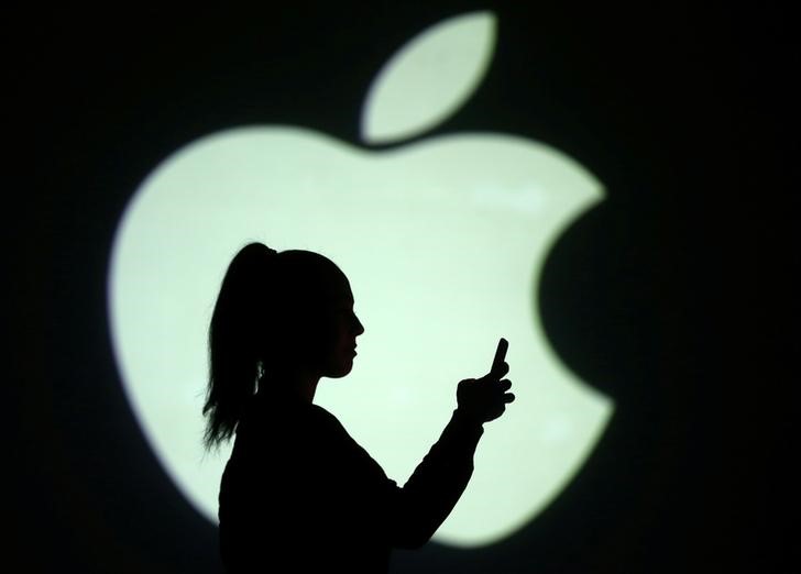 © Reuters. Silhouette of mobile user is seen next to a screen projection of Apple logo in this picture illustration