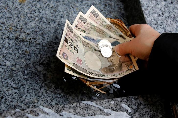 © Reuters. Посетитель храма Коами в токийском районе Нинобаси омывает водой купюры и монеты японской иены для привлечения благосостояния