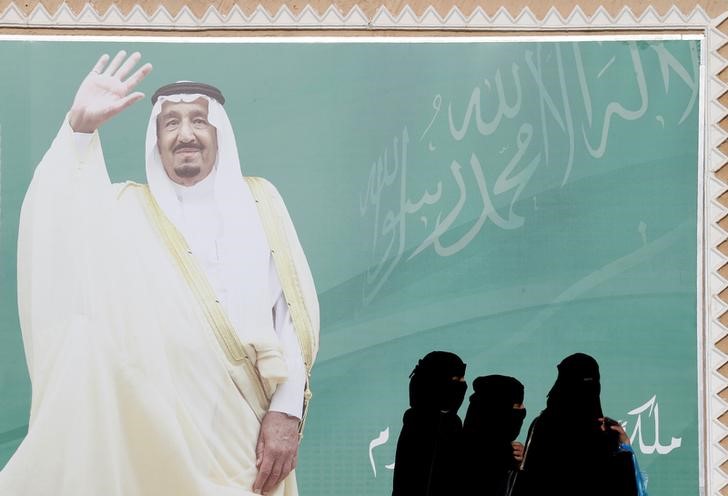 © Reuters. FILE PHOTO: Women walk past a poster of Saudi Arabia's King Salman bin Abdulaziz Al Saud during Janadriyah Cultural Festival on the outskirts of Riyadh