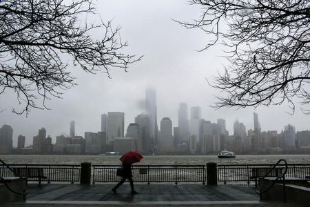 © Reuters. A woman walks during rain while the New York skyline and the One World Trade Center are seen from Exchange Place in New Jersey
