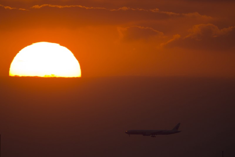 © Reuters. A passenger jet flies past the setting sun in Shanghai