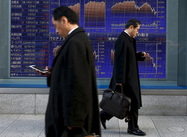 © Reuters. Men walk past an electronic board showing market indices outside a brokerage in Tokyo