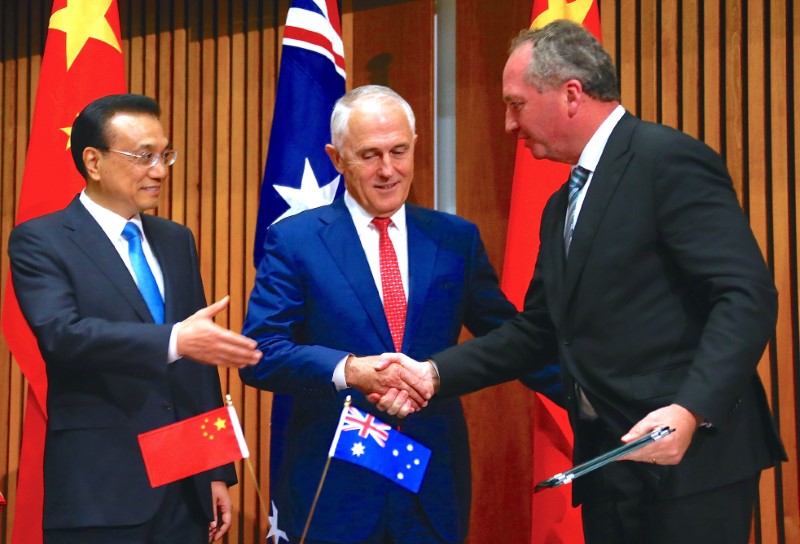 © Reuters. Chinese Premier Li Keqiang reacts as he watches Australia's Prime Minister Malcolm Turnbull shake hands with Barnaby Joyce, Australia's Deputy Prime Minister, during an official signing ceremony at Parliament House in Canberra