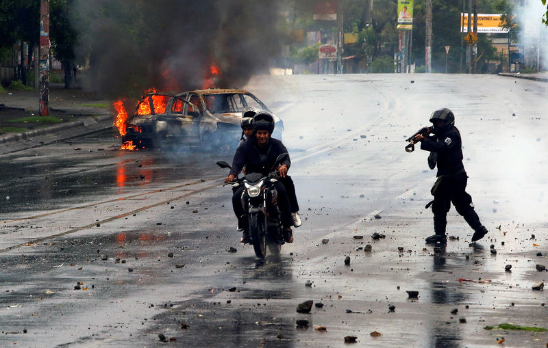 © Reuters. Policial atira contra dois homens em protesto em Manágua, na Nicarágua