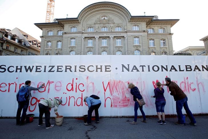 © Reuters. FILE PHOTO: Members of the sovereign money initiative, a referendum campaign that would abolish traditional bank lending and allow only money created by the central bank, clean up after spraying a slogan on the Swiss National Bank (SNB) in Bern