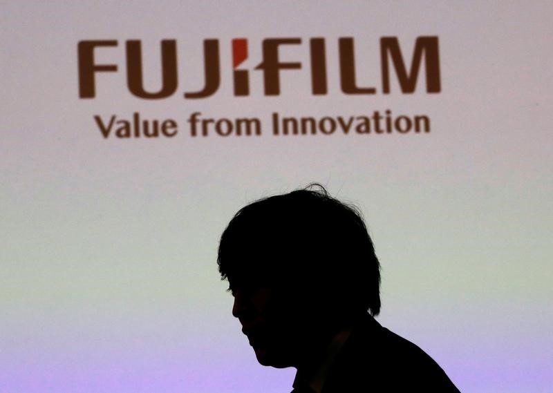 © Reuters. A man is silhouetted in front of Fujifilm Holdings' logo ahead of its news conference in Tokyo