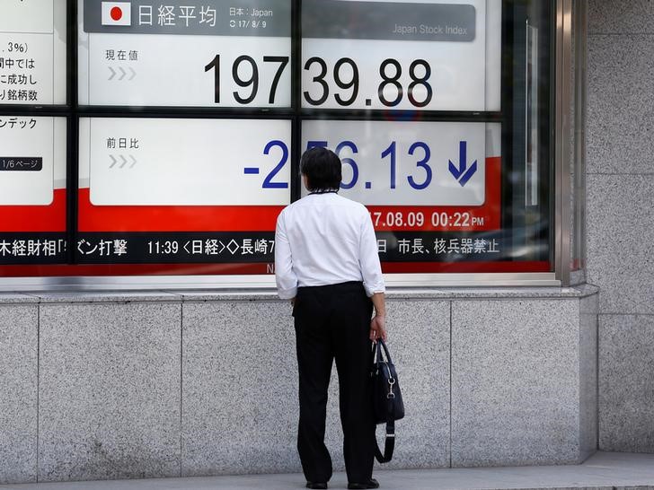 © Reuters. FILE PHOTO: A man looks at an electronic board showing Japan's Nikkei average outside a brokerage at a business district in Tokyo