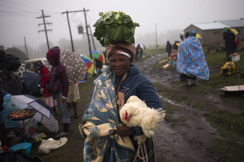 © Reuters. Local resident carries her purchases of vegetables and poultry from a makeshift market near Qunu