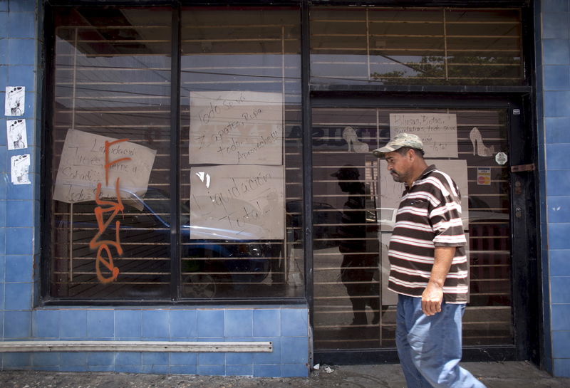 © Reuters. FILE PHOTO: A man walks past a closed store with signs reading "Closing down sale" and "Everything goes, shoes, clothes, take advantage" in Arecibo, Puerto Rico