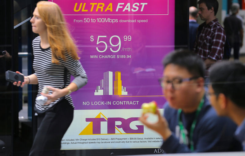 © Reuters. A woman looks at her phone as she walks past an advertisement for Australia's TPG Telecom Ltd in central Sydney, Australia