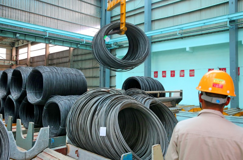 © Reuters. Worker looks on as a crane lifts a roll of steel wires at a factory in Nantong, Jiangsu