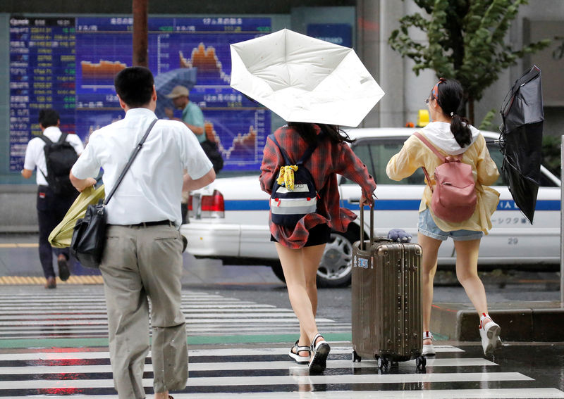 © Reuters. Passersby using umbrellas struggle against a heavy rain and wind in front of an electronic stock quotation board as Typhoon Shanshan approaches Japan's mainland in Tokyo